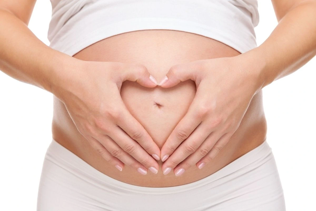 Pregnant woman holding her hands in a heart shape over her belly.